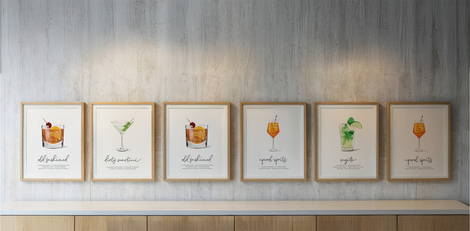 Gallery wall of hand-drawn cocktail art prints in wood frames - perfect bar cart wall decor featuring classic cocktails like Old Fashioned and Martini