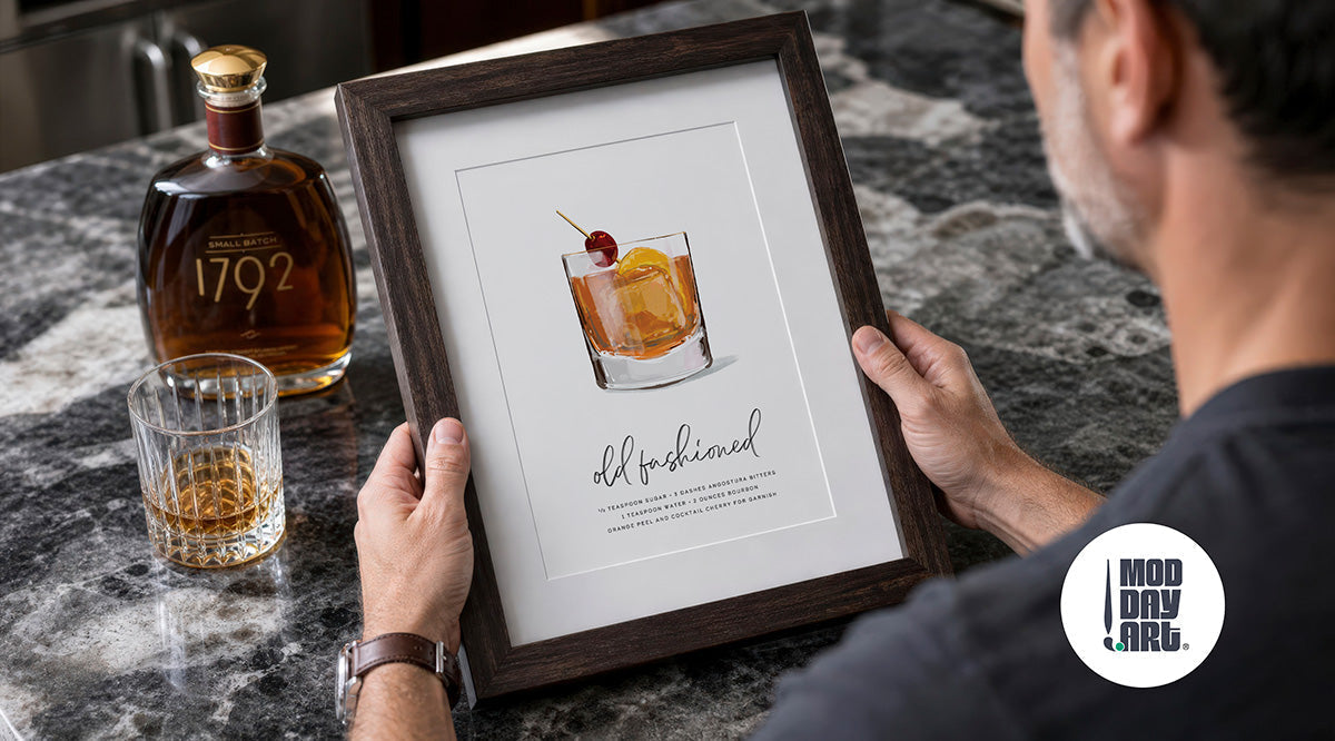 Man holding a framed Old Fashioned cocktail art print next to a bottle of 1792 bourbon, styled as a Father's Day gift idea