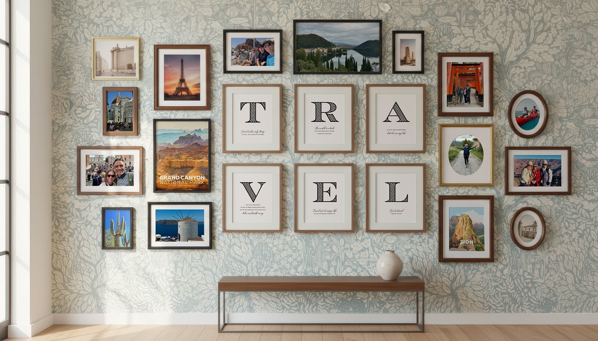 Travel-themed gallery wall combining personal vacation photos with Mod Day Art National Park posters and the TRAVEL quote letter set, displayed on floral wallpaper above a console table.
