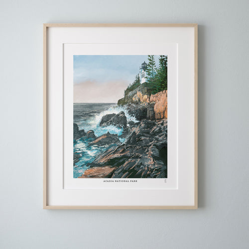 Framed artwork of Bass Harbor lighthouse on a rocky coastline with ocean waves in Acadia National Park, set against a light gray wall.