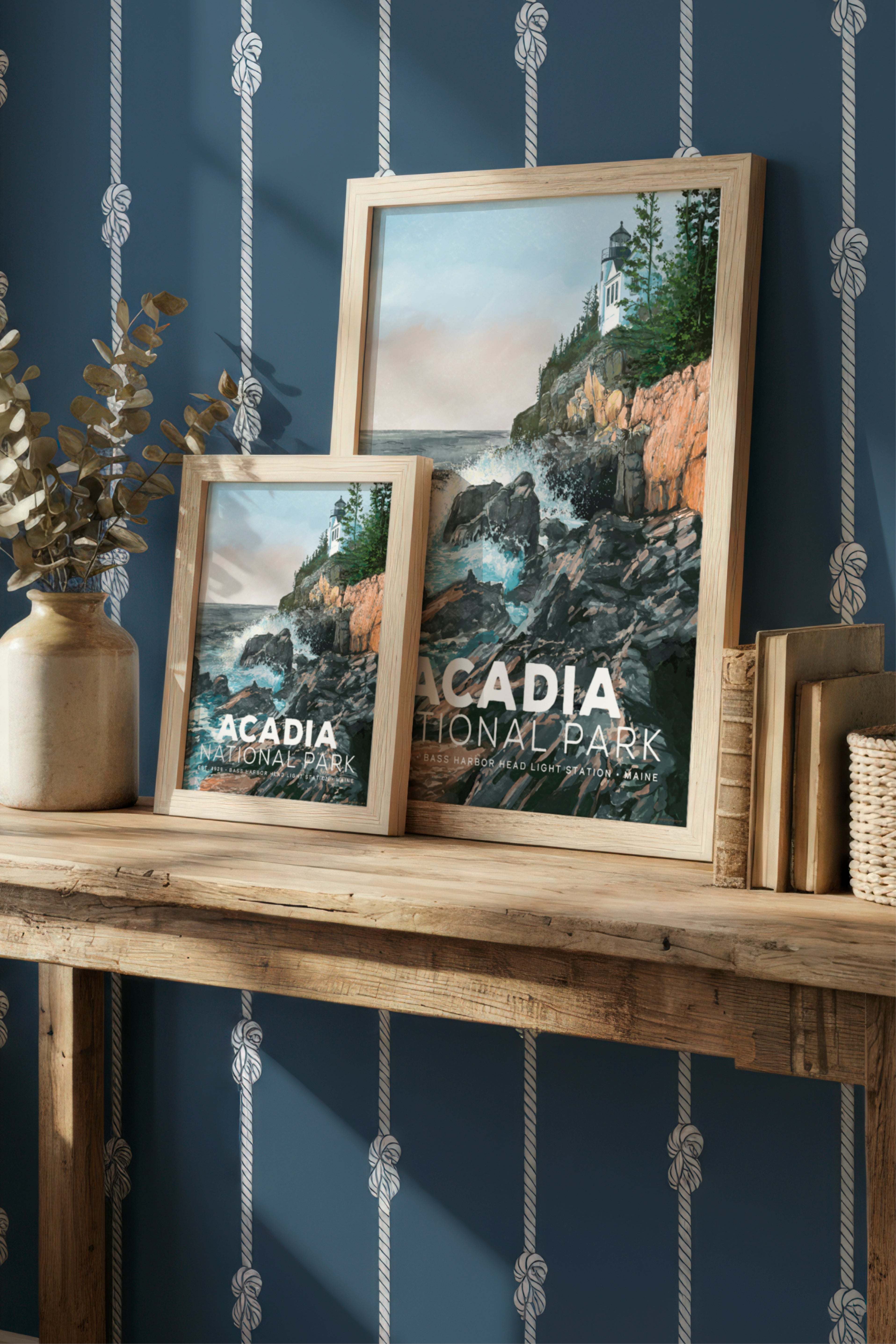 Two framed prints of Acadia National Park on a wooden shelf against a blue wall with decorative ropes.