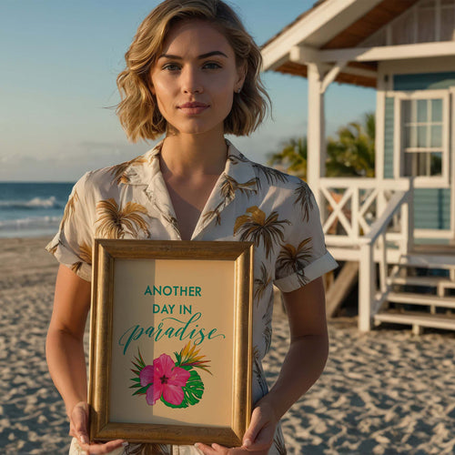 Woman holding a framed picture with 'Another Day in Paradise' text on a beach.