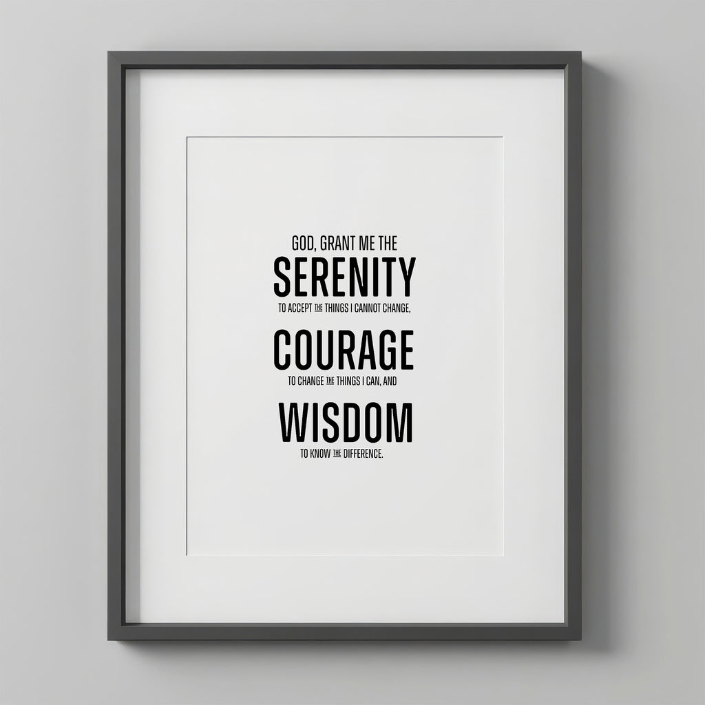 Serenity Prayer Wall Art print in a charcoal-gray frame with a white mat, hung on a light gray wall. The prayer is set in bold modern block type, with SERENITY, COURAGE, and WISDOM in large caps.
