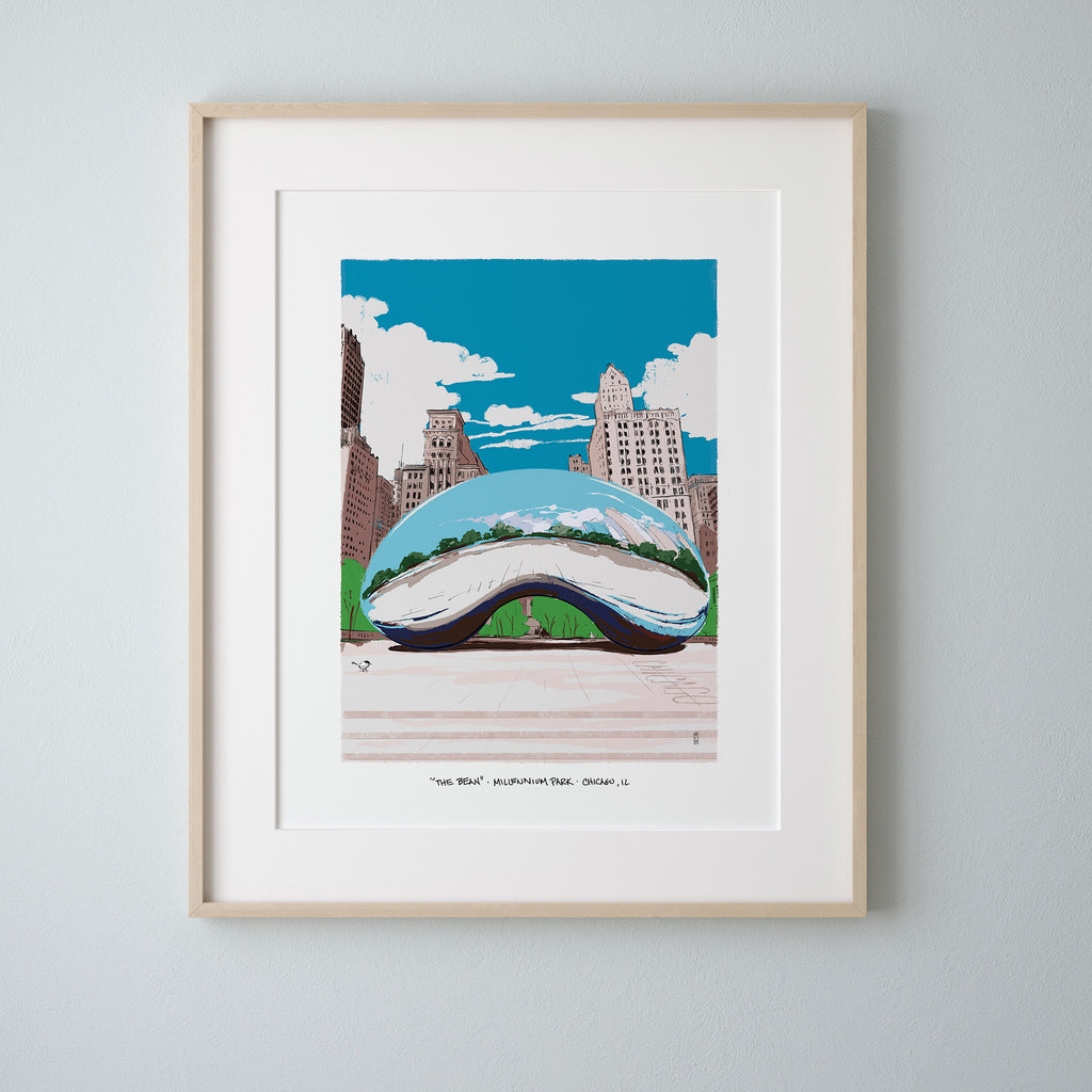A framed art print of Cloud Gate in Chicago's Millennium Park, matted in white with a light wood frame, hung on a light gray wall.