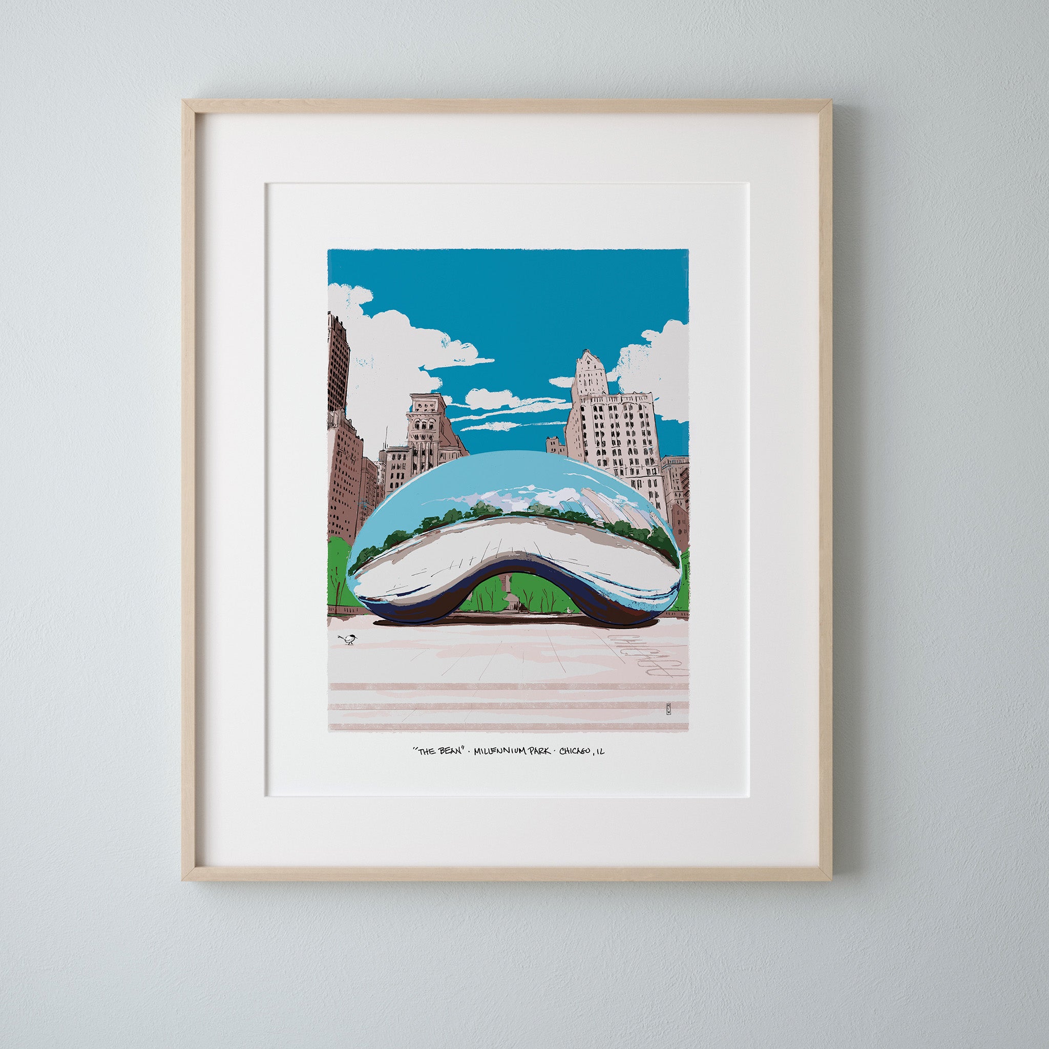 A framed art print of Cloud Gate in Chicago's Millennium Park, matted in white with a light wood frame, hung on a light gray wall.