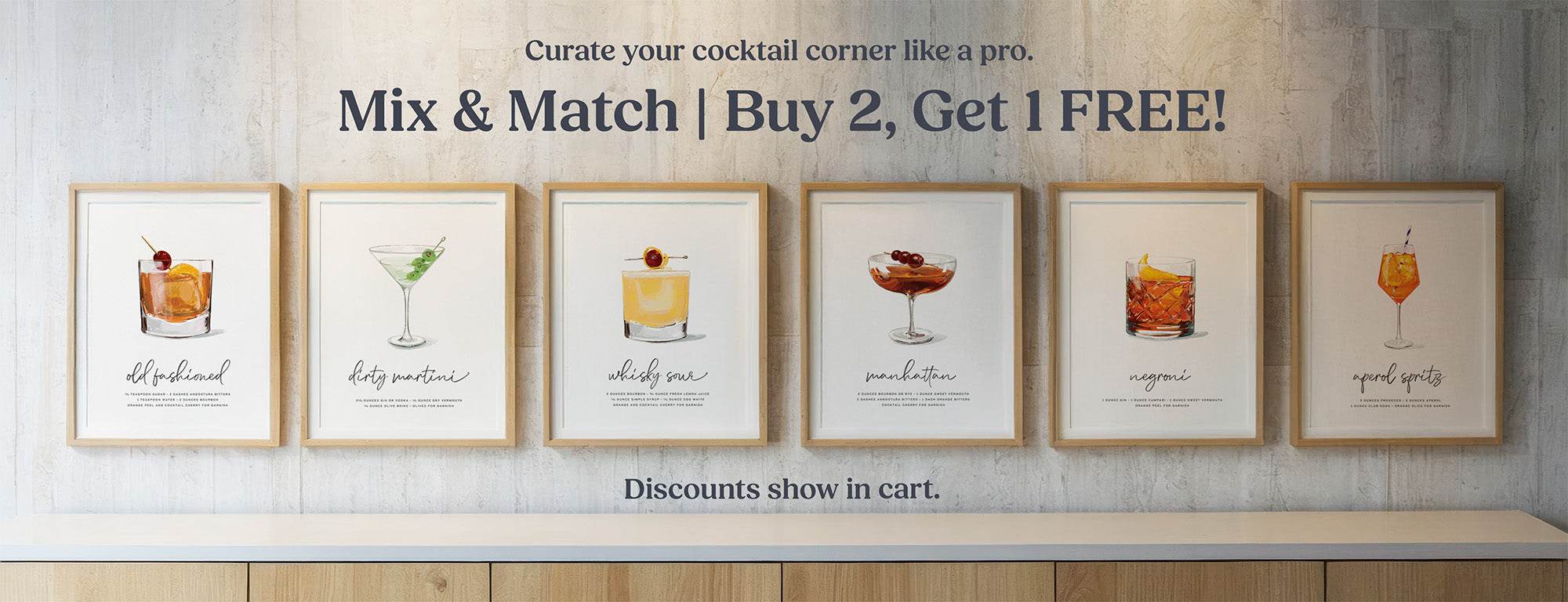 Framed cocktail wall art illustrations on a wall with promotional text for a buy two, get one free offer.