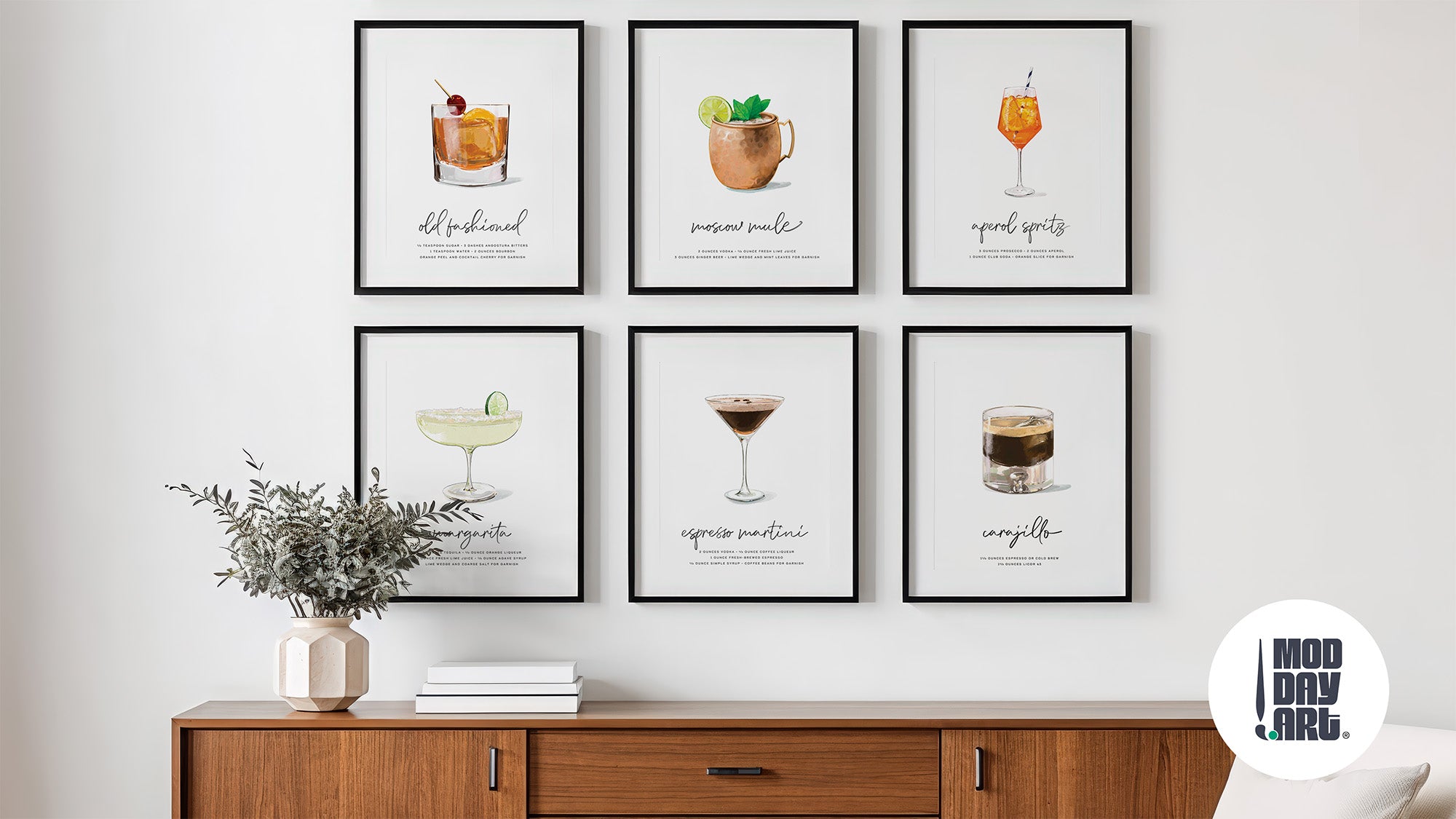 Hand-illustrated cocktail wall art displayed as a gallery wall—six black-framed prints showing Old Fashioned, Moscow Mule, Aperol Spritz, Margarita, Espresso Martini, and Carajillo recipes above a walnut credenza with eucalyptus arrangement