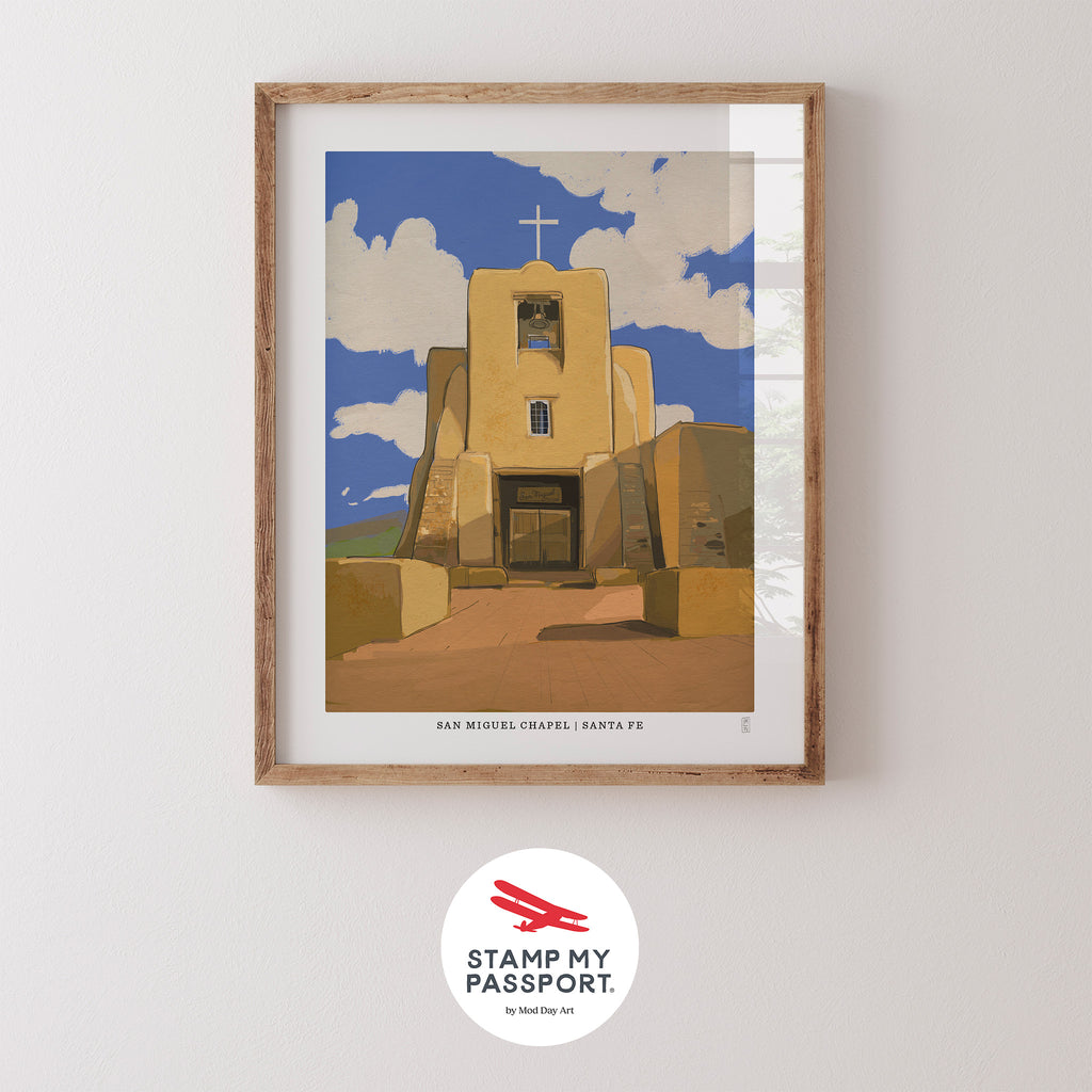 Framed Hand-signed  Art Print of San Miguel Chapel in Santa Fe, New Mexico with a blue sky and clouds, on a white wall with 'Stamp My Passport' logo.