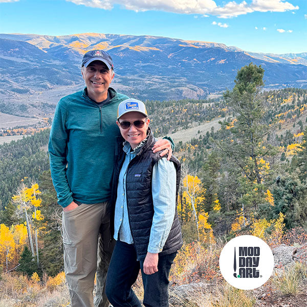 Mod Day Art creators standing on a mountain with scenic view and 'Mod Day Art' logo.