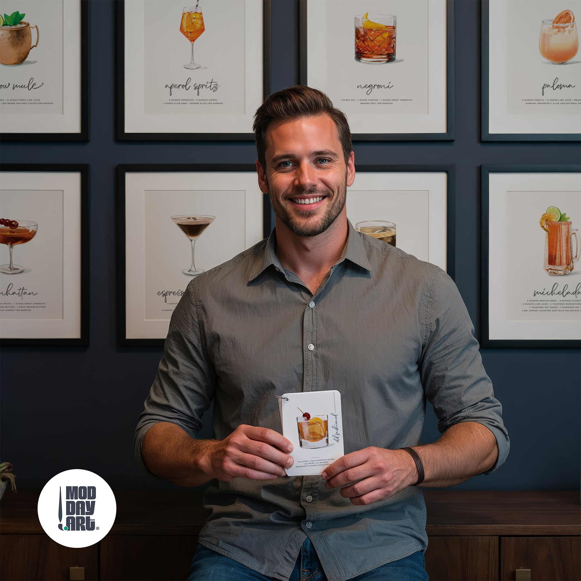Man holding cocktail recipe cards in front of gallery wall of vintage cocktail poster collection