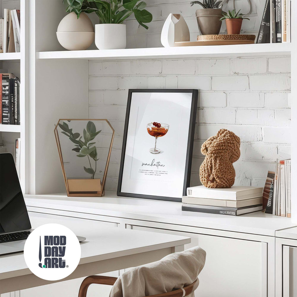 Modern office desk with decor items and a framed Manhattan recipe cocktail wall art on a white brick wall background.