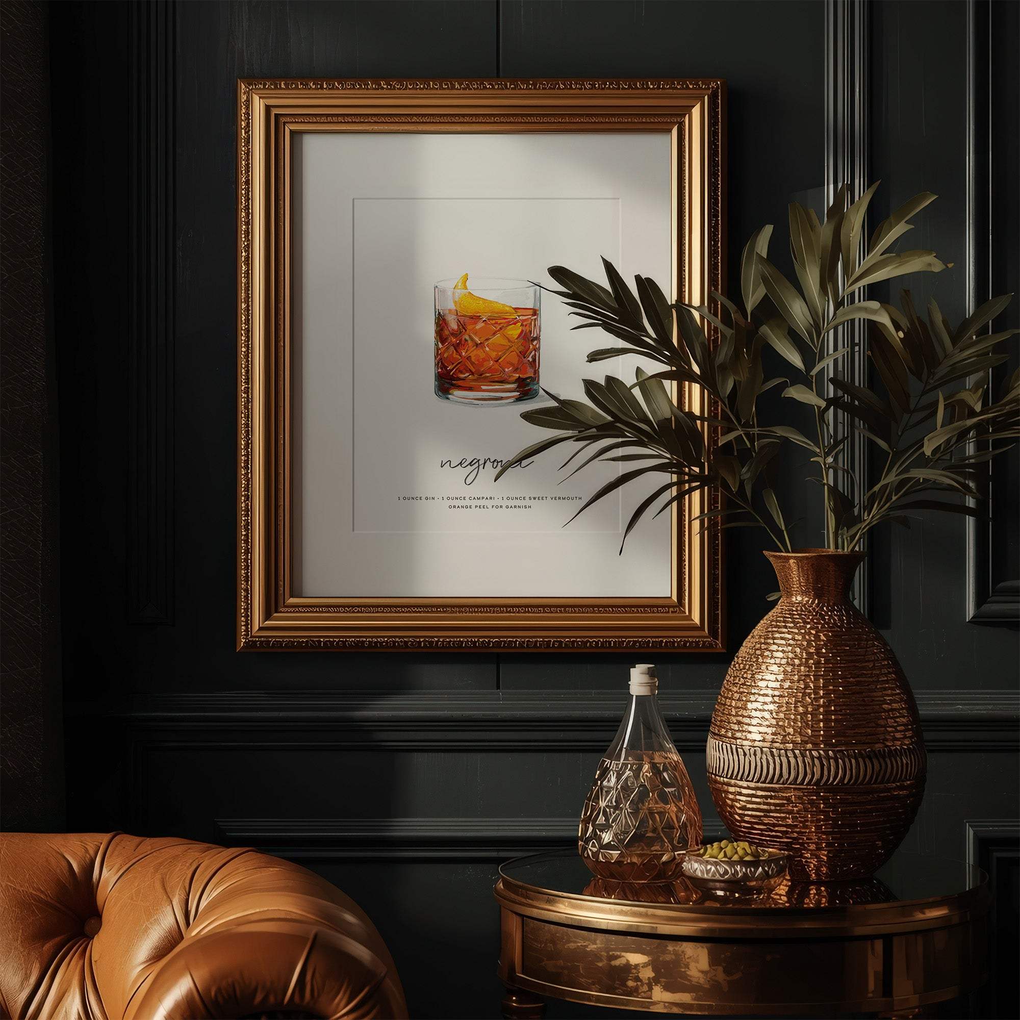 Framed Negroni cocktail recipe wall art in ornate gold frame displayed on dark paneled wall above vintage leather chair and round side table with decorative vase and glassware.