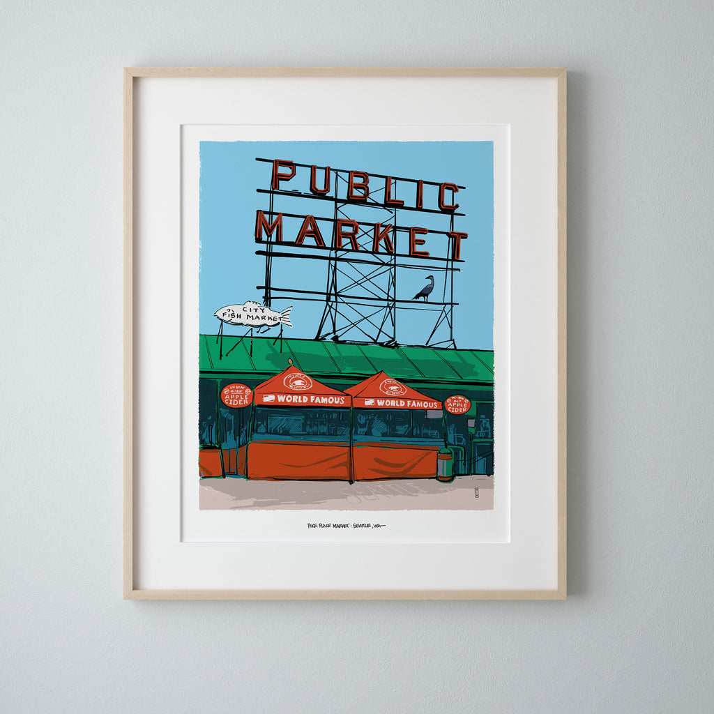 A framed city art print depicting a stylized Seattle 'Public Market' sign and market stall scene, mounted on a light gray wall.