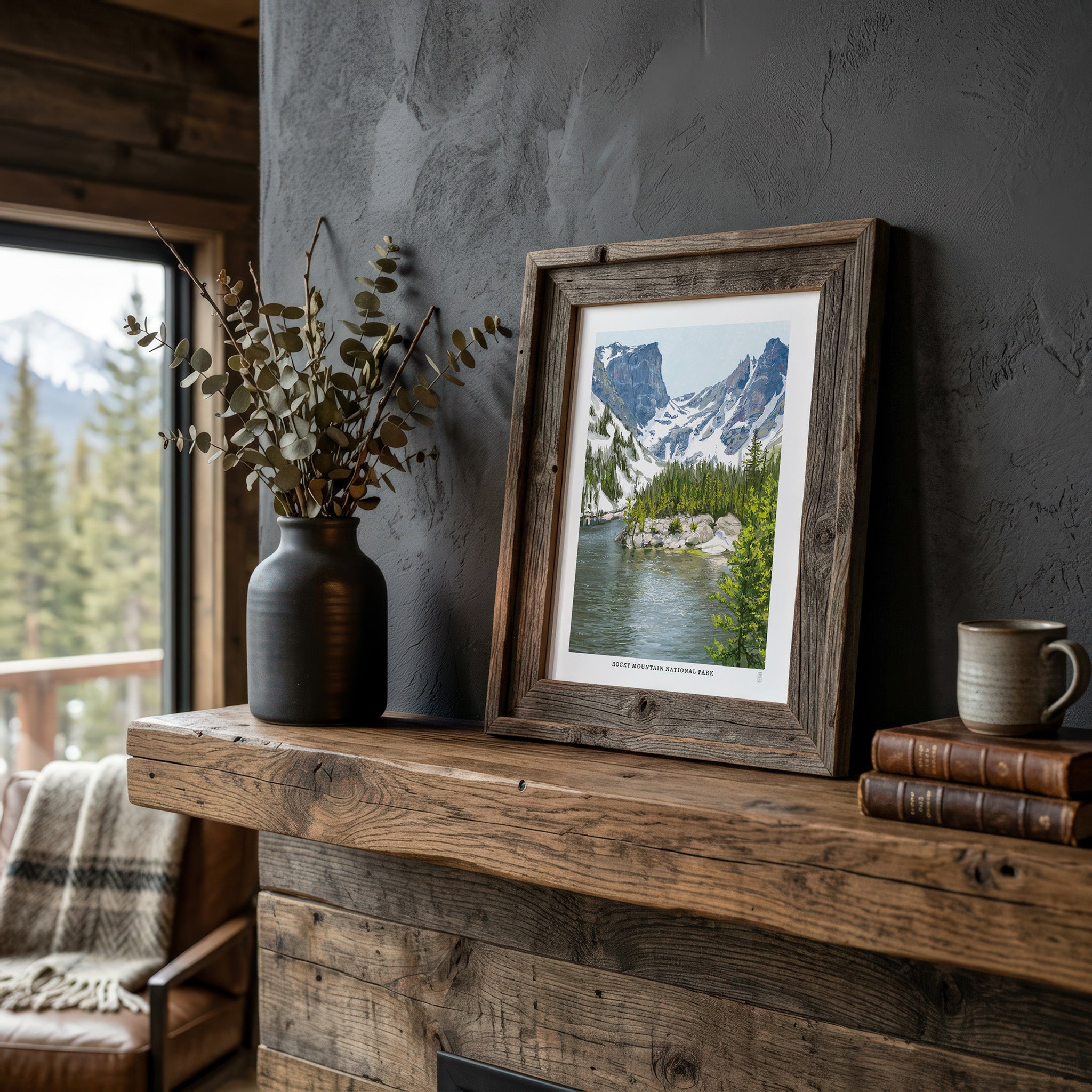 Framed Rocky Mountain National Park landscape print on a wooden mantelpiece with a vase and books.