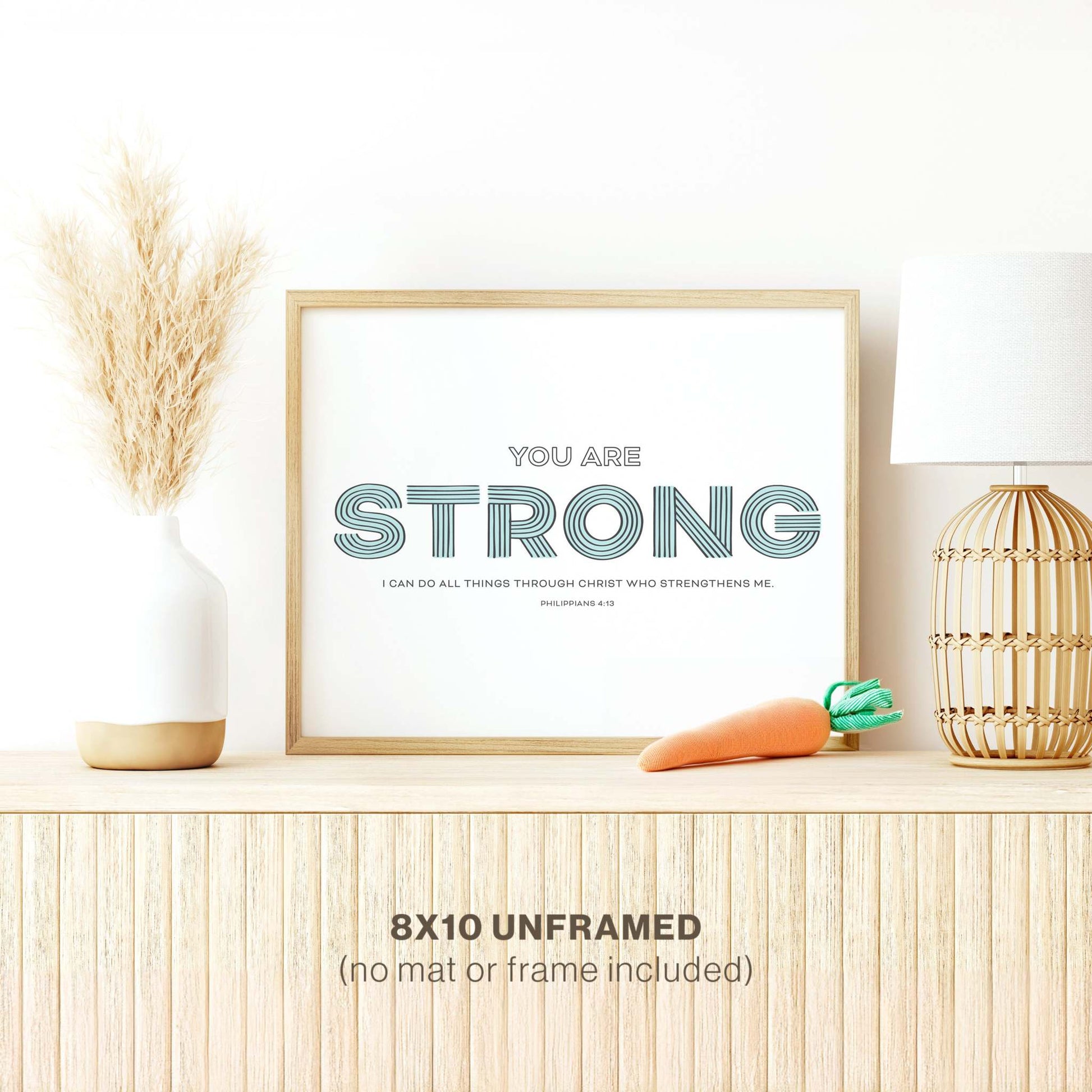 The Scriptionery™ “Strong” nursery art print displayed in a modern wood frame, accented with stylish home decor accessories for a modern touch.