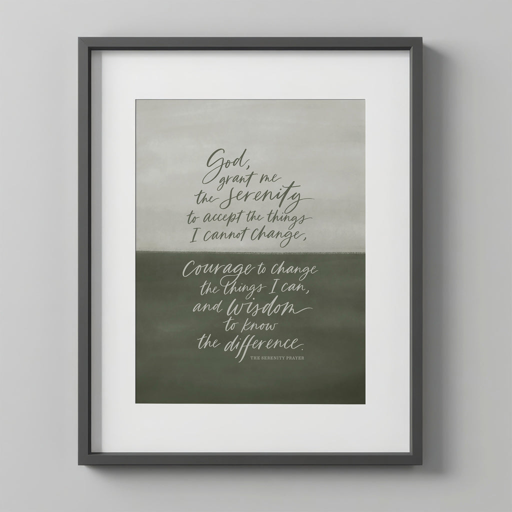 Serenity Prayer Wall Art print in the Sage colorway, in a charcoal frame with a white mat on a light gray wall. The print has a hand-painted sage-to-olive green gradient background with the prayer hand-lettered in white script.