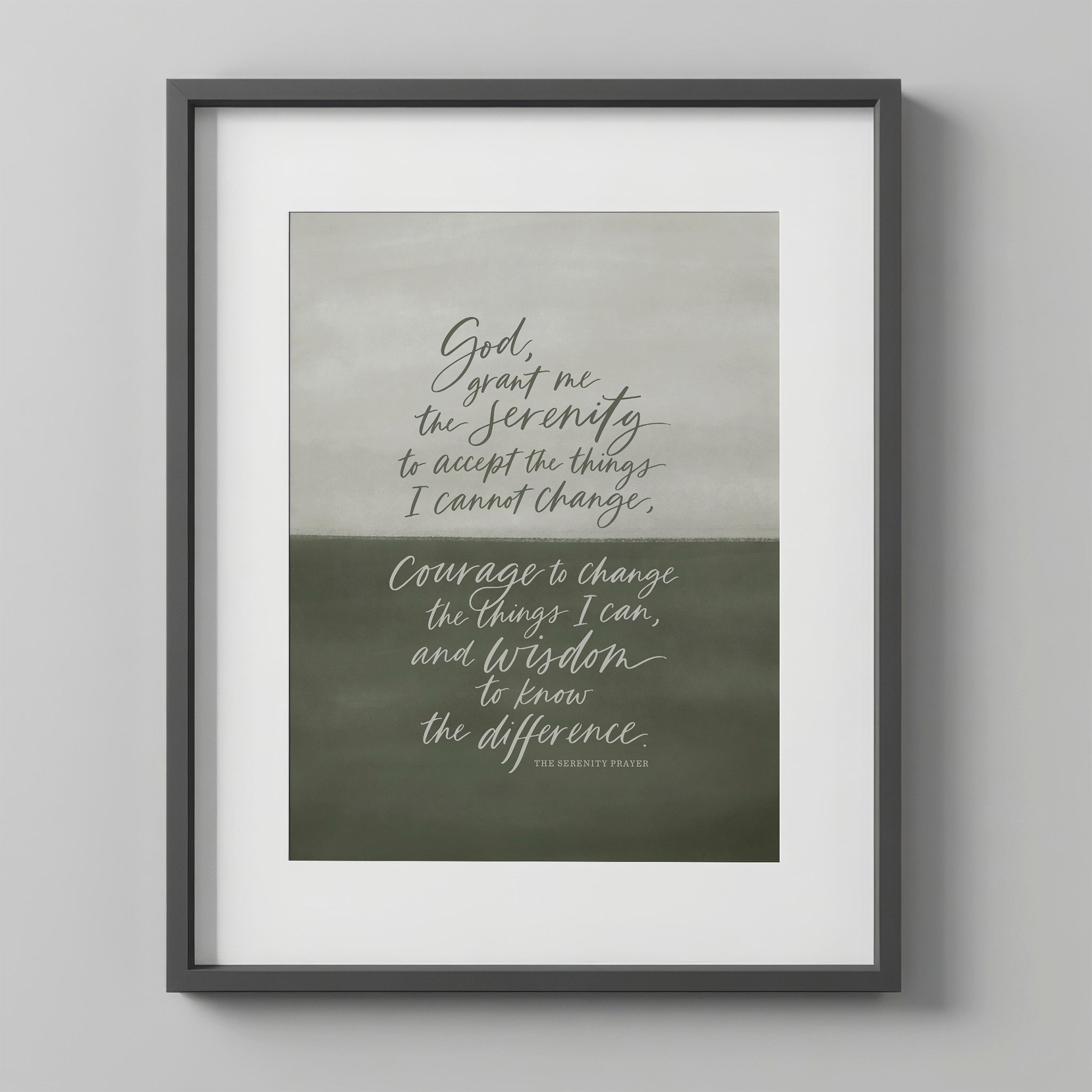 Serenity Prayer Wall Art print in the Sage colorway, in a charcoal frame with a white mat on a light gray wall. The print has a hand-painted sage-to-olive green gradient background with the prayer hand-lettered in white script.