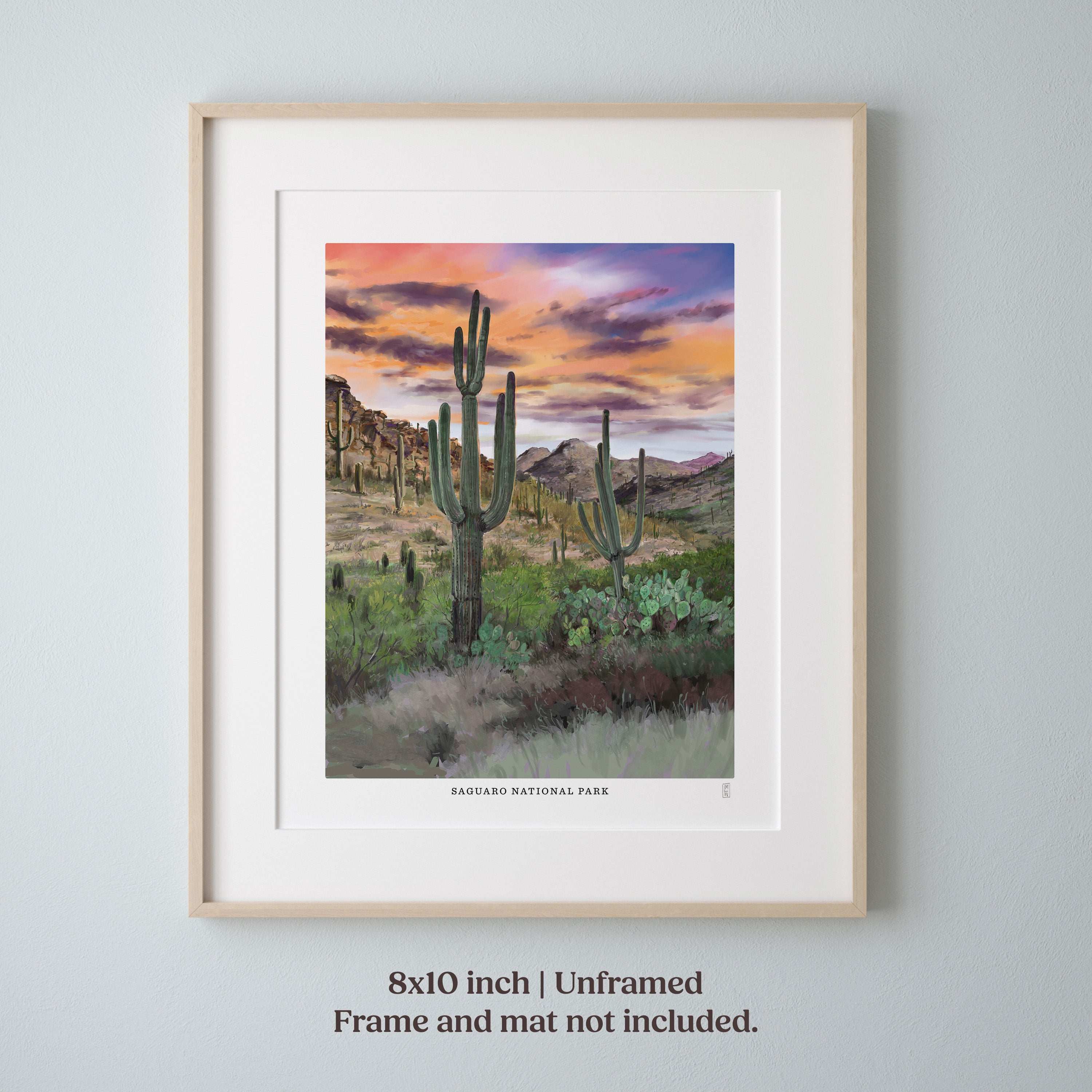 Framed Saguaro National Park hand-signed desert landscape print with cacti and sunset sky on a gray wall.