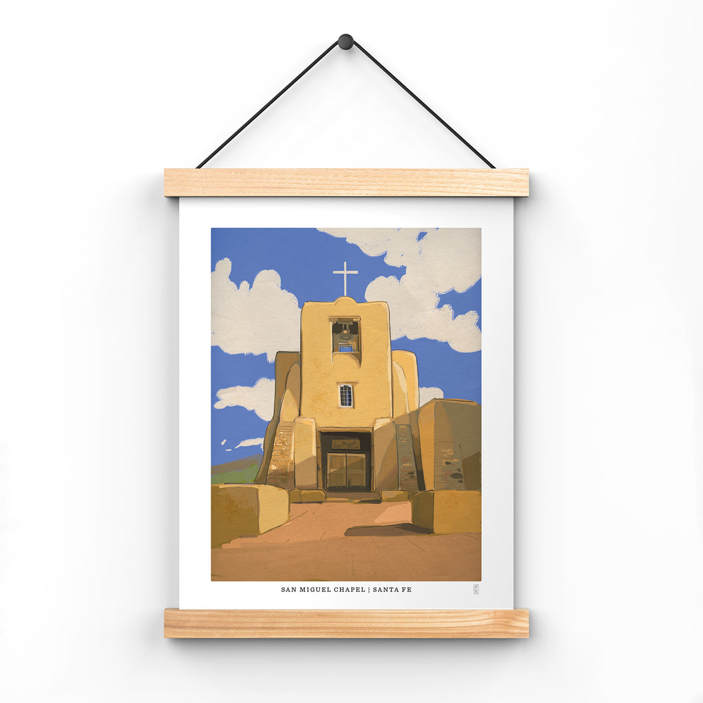 Hand-signed travel Art Print of San Miguel Chapel in Santa Fe, New Mexico in poster hangar with a blue sky and clouds, displayed on a white background.