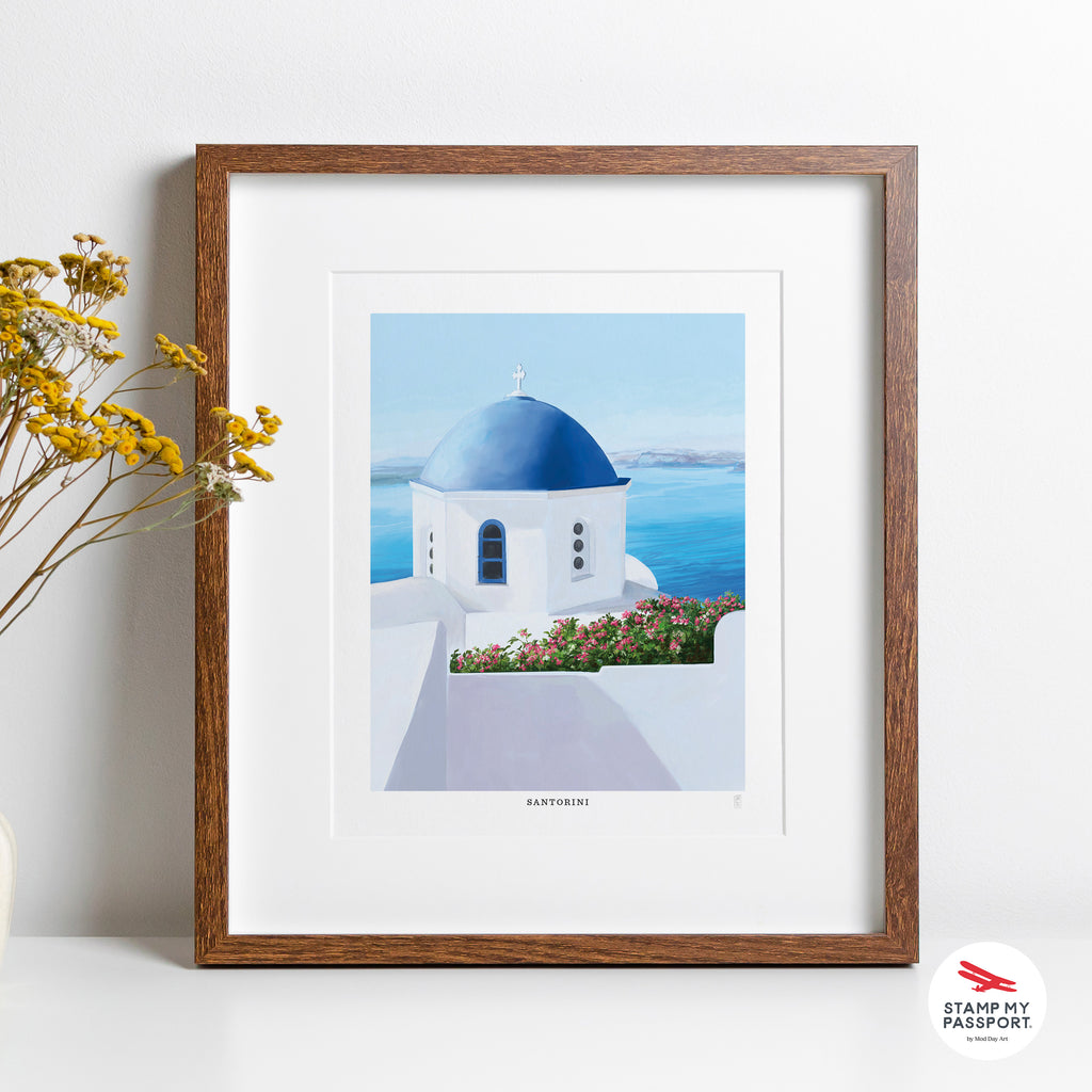 Framed hand-signed art print of a Santorini blue-domed church with ocean view on a white wall.