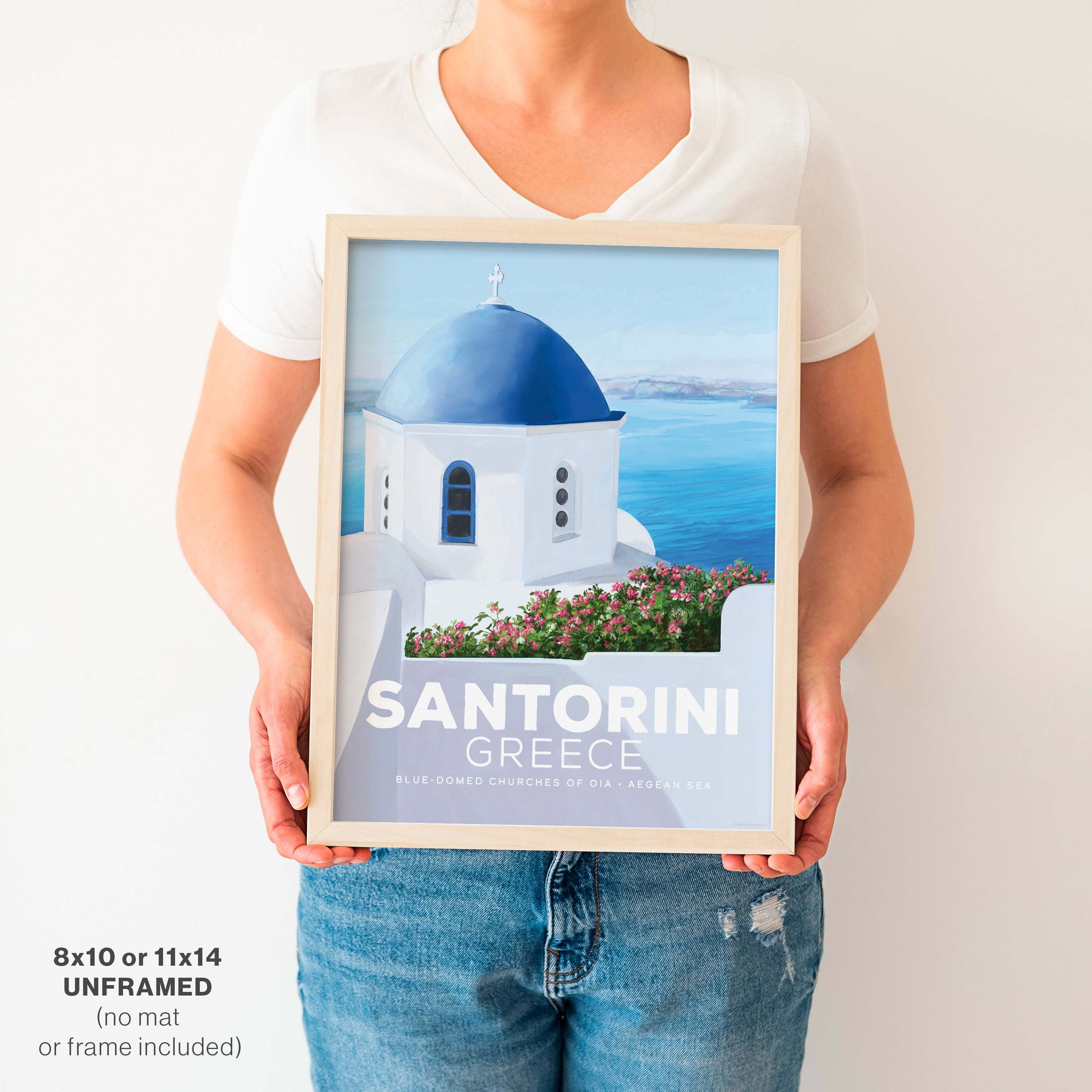 Woman in a white t-shirt holding an 11x14 inch Santorini, Greece vintage city poster featuring the iconic blue-domed churches.