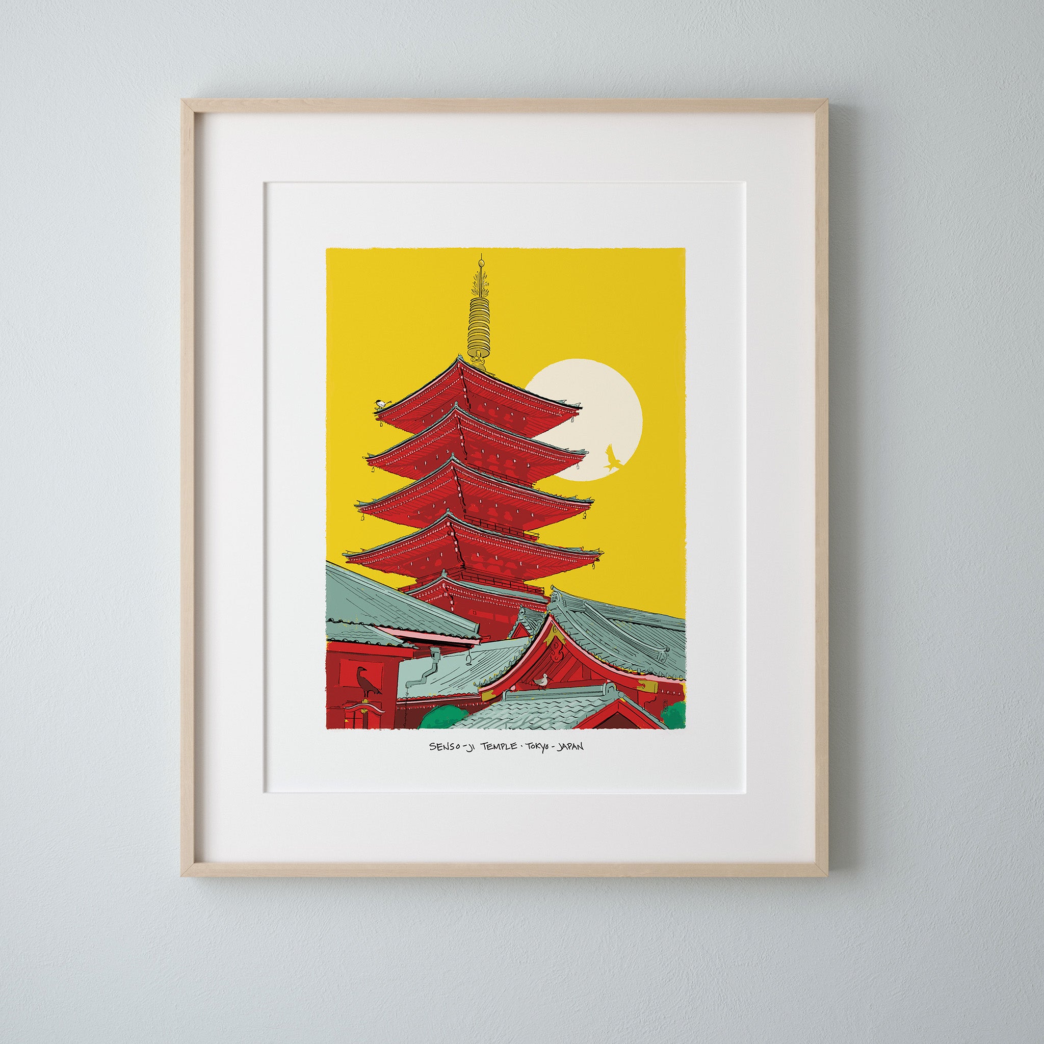 A framed art print of Senso-ji Temple's pagoda in Tokyo, matted in white with a light wood frame, hung on a light gray wall.