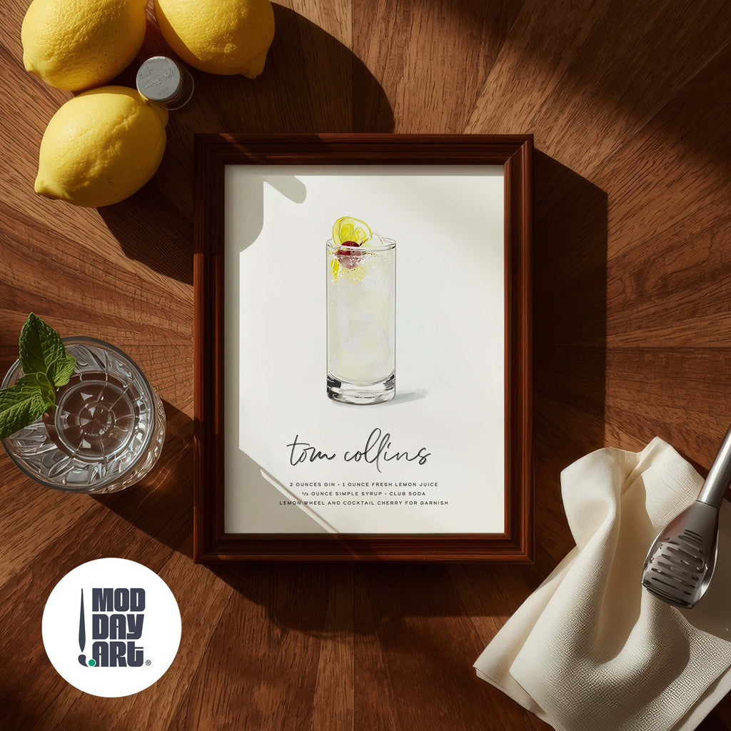 Framed Tom Collins Cocktail Wall Art on a wooden table with lemons and a cocktail shaker.