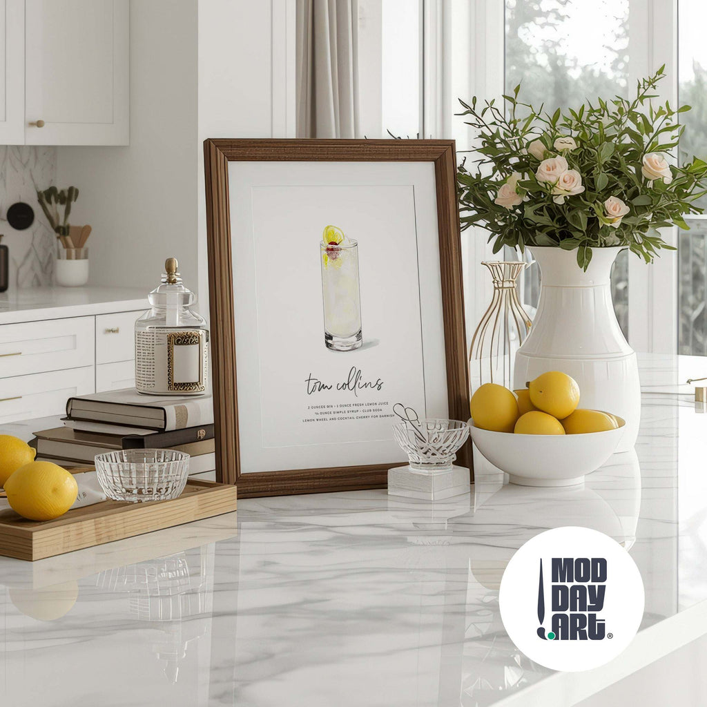 Decorative setup with a framed Tom Collins Cocktail Wall Art, vase with flowers, and lemons on a marble surface, featuring the 'MOD DAY ART' logo.
