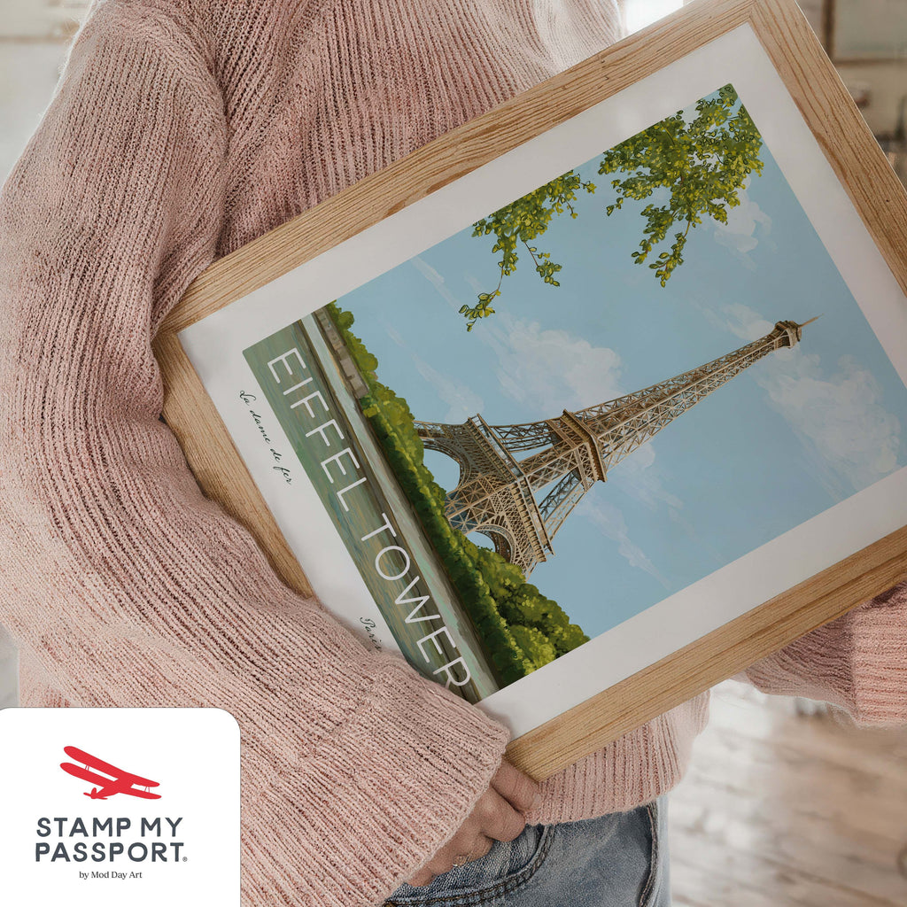 Person holding a travel wall art print with Eiffel Tower illustration, wearing a pink sweater.