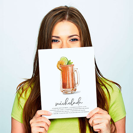 Woman holding michelada recipe cocktail wall art in front of her face.